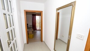 Un pasillo con un espejo grande y una puerta que da a una habitación con ventana y una pequeña mesa.