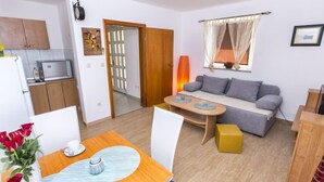 Un espacio habitable compacto con comedor, sofá, cocina y puerta que da a un balcón.