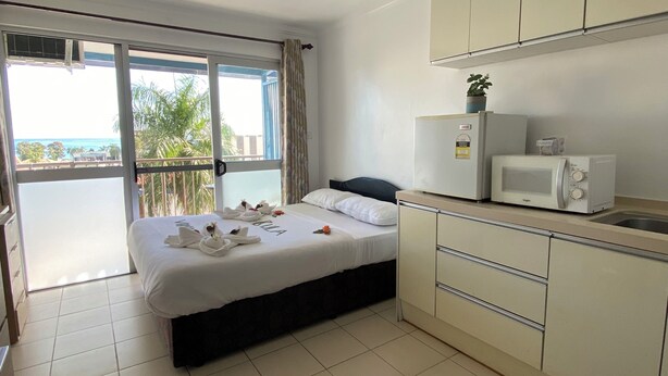 Une chambre d’hôtel avec un lit, une kitchenette et un balcon donnant sur l’océan.