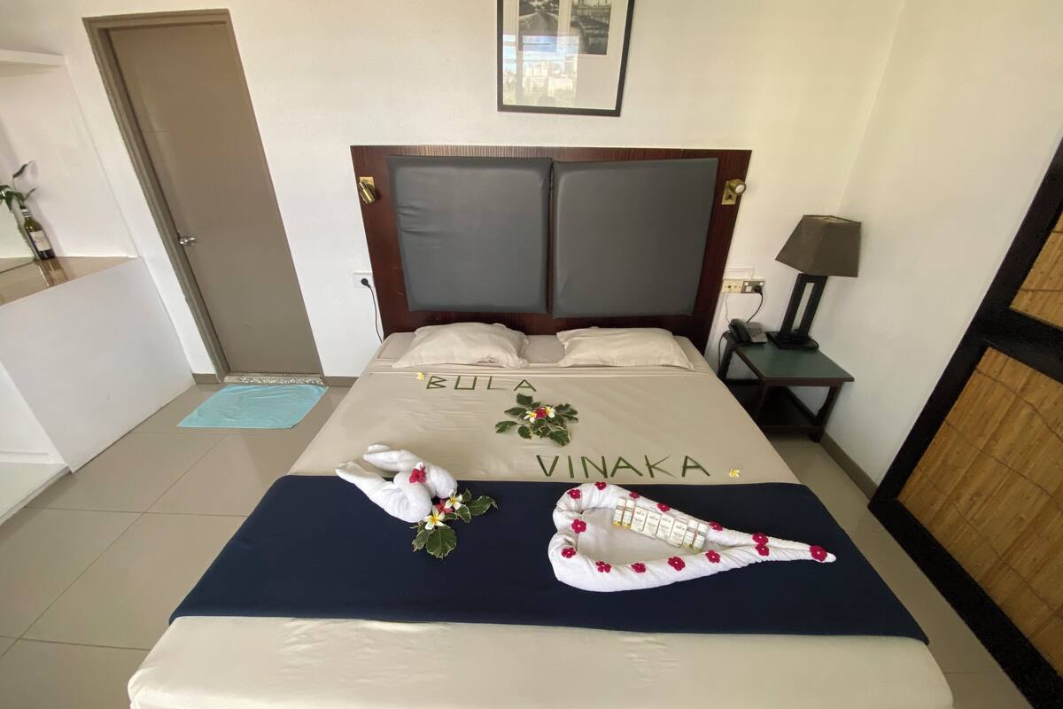 A neatly made bed with a headboard, a bedside table with a lamp, and a framed picture on the wall.