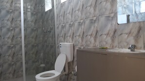Une salle de bain avec un mur en marbre, des toilettes, une douche et un lavabo.