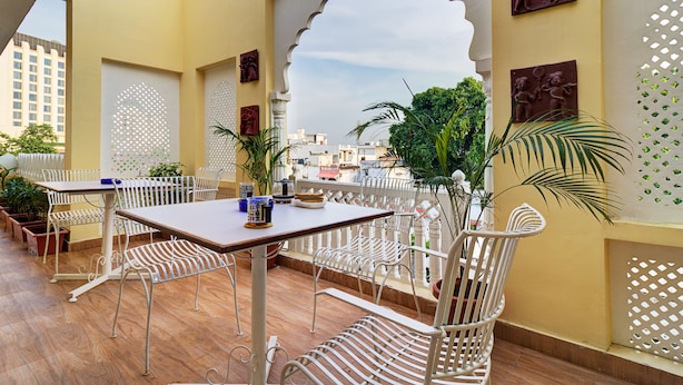 A terrace with white metal furniture, a wooden table, and potted plants. - Ashapura Niwas by Vista Rooms (Jaipur)