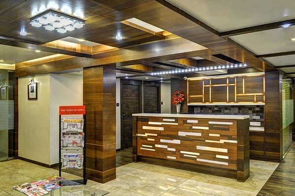 Zona de recepción con un mostrador de madera, un soporte para periódicos y un cuadro en la pared.