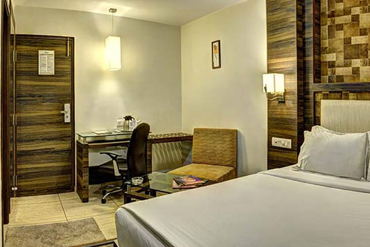 A hotel room with a bed, a desk, a chair, and a wall with a textured pattern.