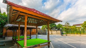 A covered seating area with a thatched roof, benches, and a paved ground. - OYO 1427 Azzahra Guest House Syariah (Mataram)