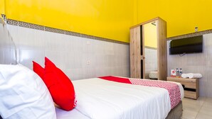 A hotel room with a bed, a wooden wardrobe, a TV, and a small table with toiletries. - OYO 1427 Azzahra Guest House Syariah (Mataram)