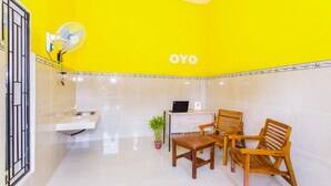 A bright yellow room with a sink, two wooden chairs, a laptop on a desk, and a fan mounted on the wall. - OYO 1427 Azzahra Guest House Syariah (Mataram)
