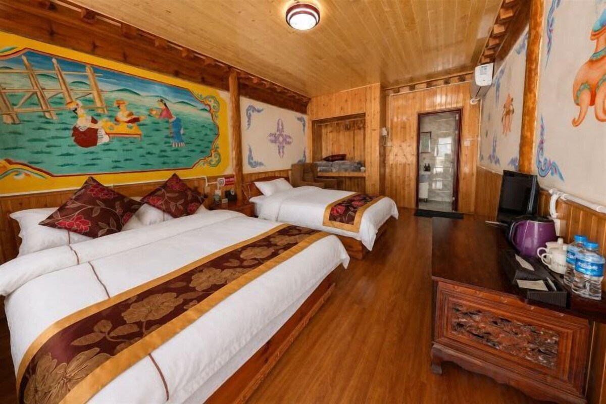 A hotel room with two beds, wooden flooring, a mural on the wall, and a television on a wooden cabinet.