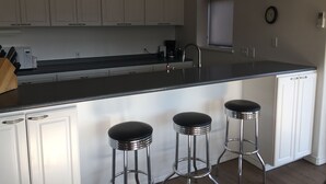 A modern kitchen with white cabinets, a black countertop, and three bar stools. - Kendall Yards Home - Stunning views, amazing downtown location (Spokane)