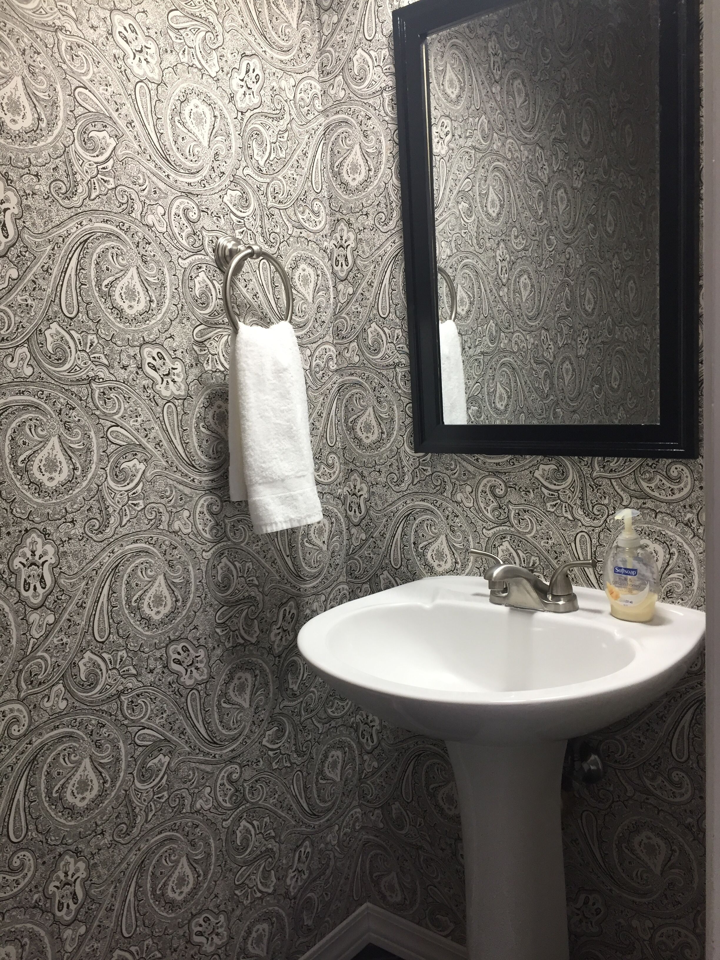 Un baño con lavamanos blanco, un espejo y una toalla colgada en un perchero.