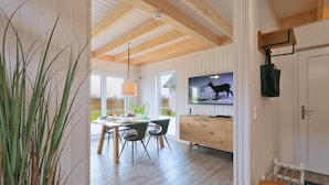 A modern dining area with a wooden ceiling, a TV mounted on the wall, and a view of the outdoors through large windows.