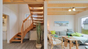 A cozy living room with a wooden staircase, a wicker chair, a small table, and a painting on the wall.