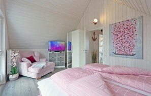 Een slaapkamer met een roze bed, een televisie, een roze fauteuil en een kunstwerk aan de muur.