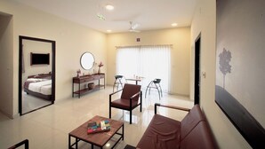 A modern hotel room with a large mirror, a flat-screen TV, a sofa, a coffee table, and a dining area with a table and chairs. - Purple Cloud Urban (Bengaluru)