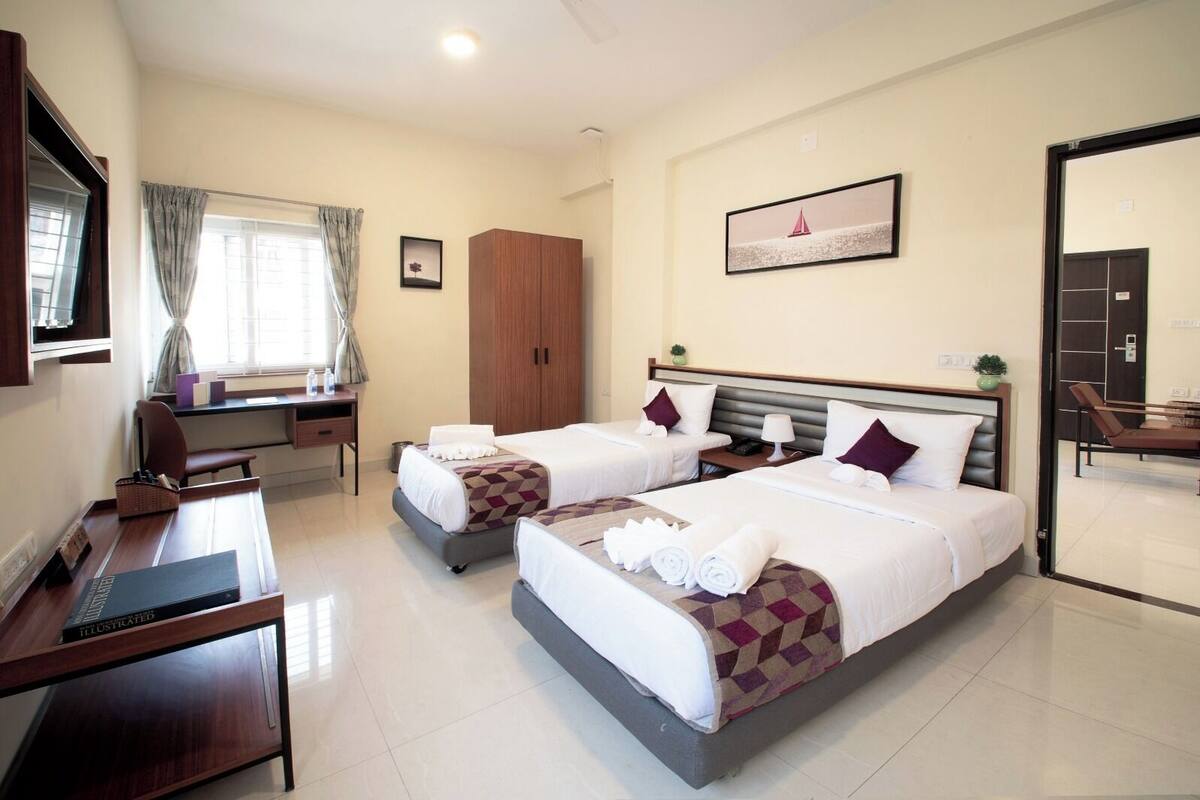 A hotel room with two beds, a desk, a chair, a wardrobe, and a window with curtains.