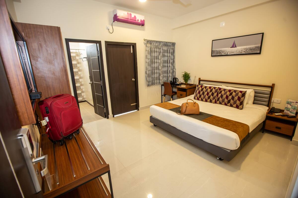 A hotel room with a bed, a desk, a chair, a suitcase, and a door.