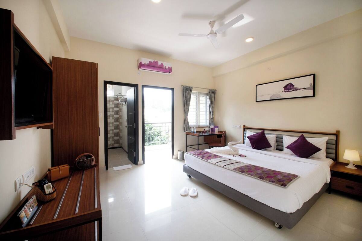 A hotel room with a bed, a desk, a chair, a TV, and a balcony.
