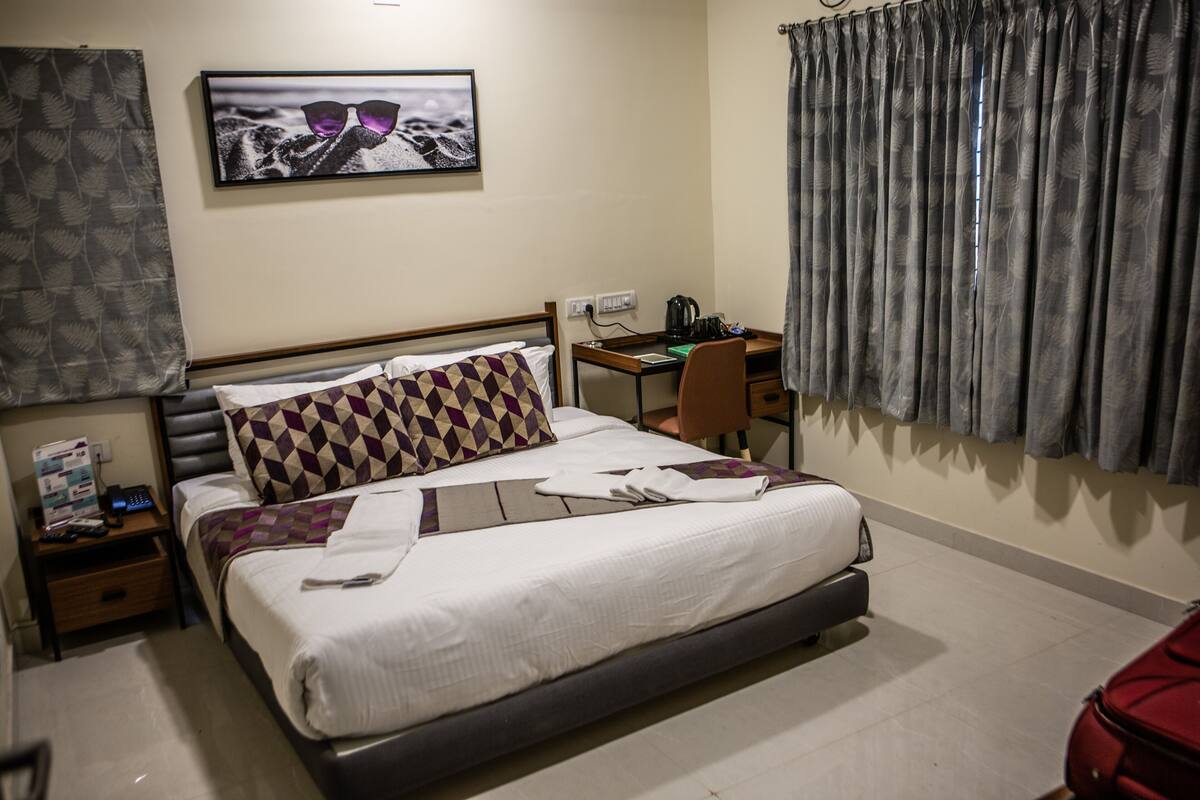 A hotel room with a bed, a desk, a chair, a television, and a window with curtains.