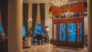 A lobby with a grand piano, a chandelier, and a view of the city through large doors. - Atlas Oteli (Izmir)