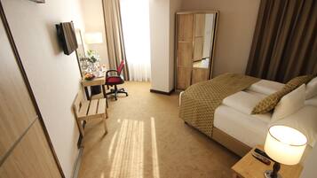 Una habitación de hotel con una cama, un escritorio con una silla, un espejo, una lámpara y un televisor en la pared.