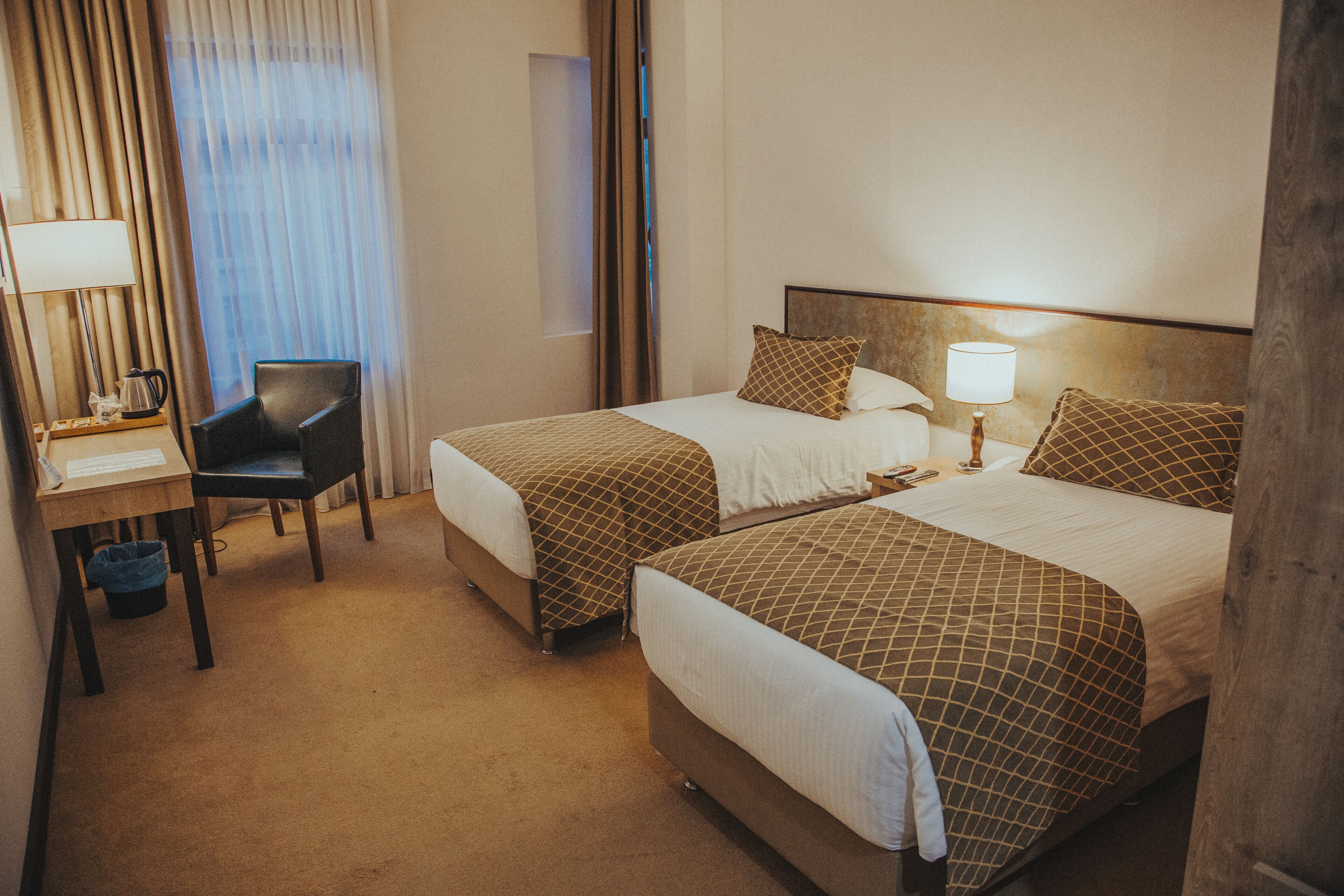 Una habitación de hotel con dos camas, un escritorio, una silla y una lámpara.
