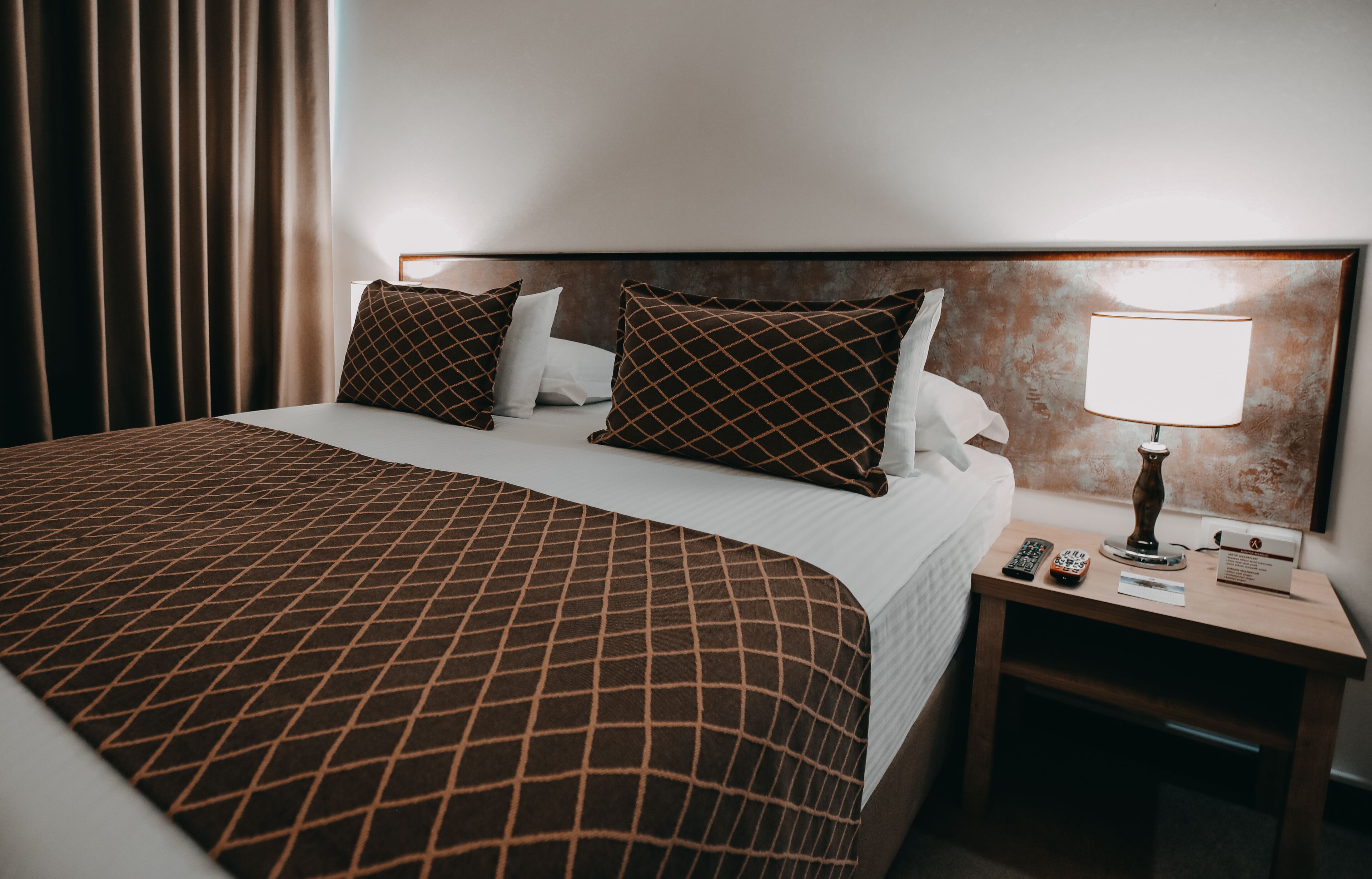 Una habitación de hotel con una cama grande, una mesita de noche con lámpara y un teléfono.