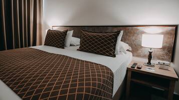 Una habitación de hotel con una cama grande, una mesita de noche con lámpara y un teléfono.
