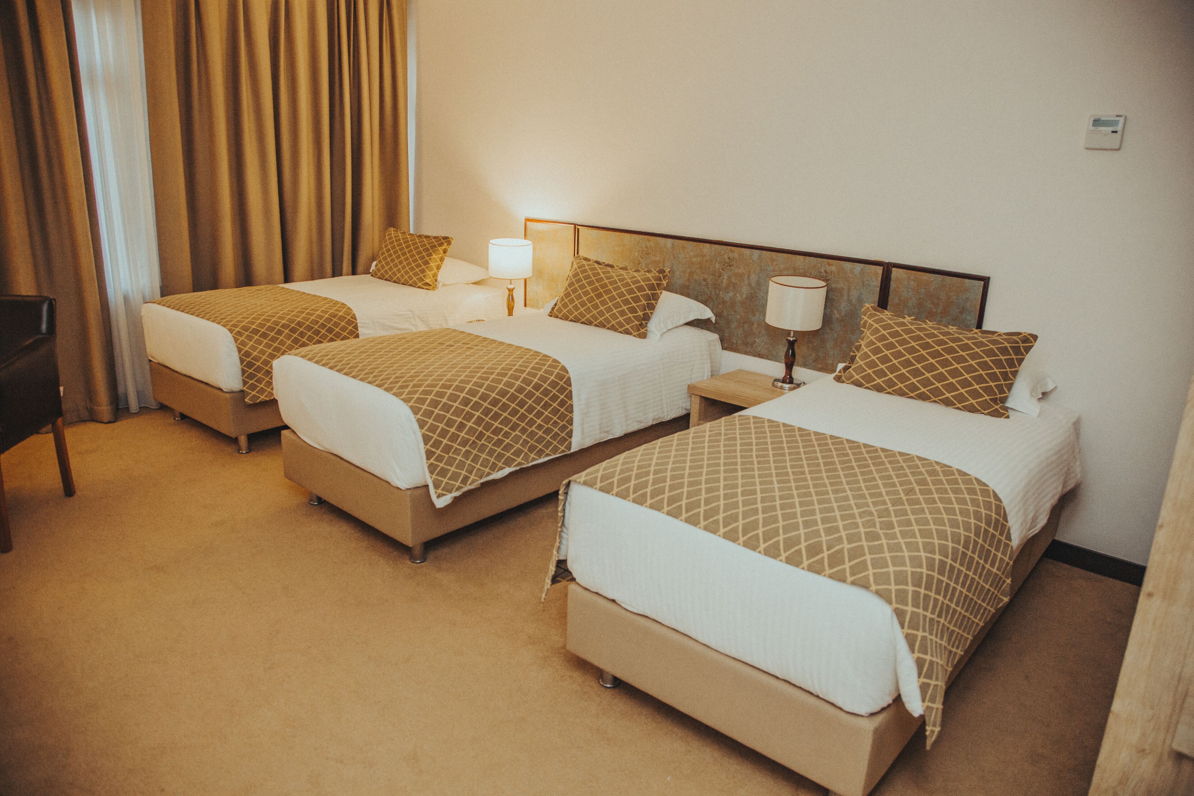 Ein Hotelzimmer mit drei Betten, jeweils mit Kopfteil, Nachttischen und Lampen.