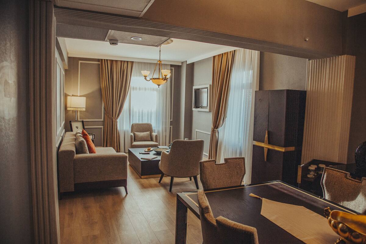 A hotel room with a sofa, armchairs, a dining table, a TV, and a chandelier.
