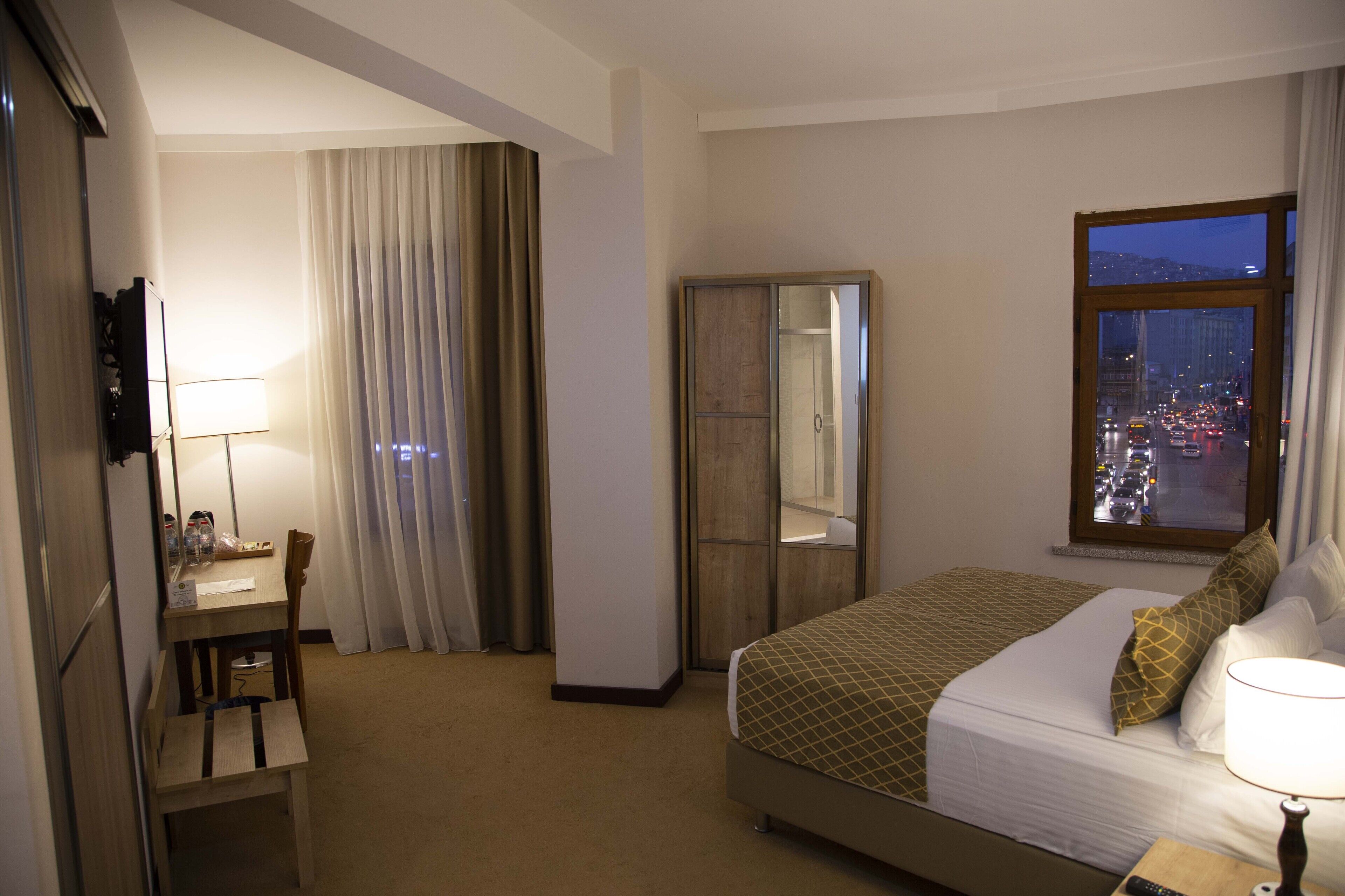 Habitación de hotel con cama, escritorio, silla, armario y ventana con vista a la ciudad.