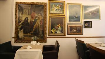 Un comedor con una mesa dispuesta para dos, un cuadro grande en la pared y varias obras de arte enmarcadas.