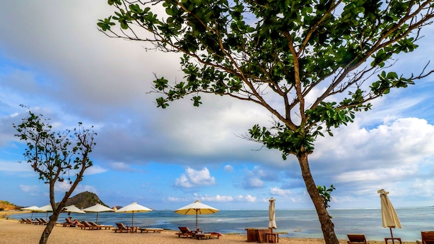 A beach with lounge chairs and umbrellas, a clear sky, and a calm sea. - OYO 1514 Rara Inn (Kuta)