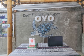 A table with a laptop, a book, and a poster on a patterned tablecloth. A wall mural with a turtle and the text "Don't Forget To Enjoy! OYO" is visible. - OYO 1514 Rara Inn (Kuta)