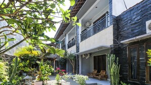 A two-story building with a balcony, surrounded by lush greenery and various plants. - OYO 1514 Rara Inn (Kuta)