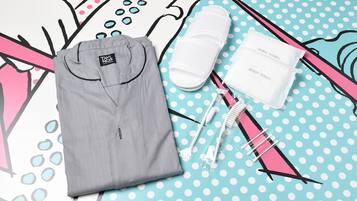Une chemise grise soigneusement pliée, deux serviettes de bain blanches et une trousse de brosses à dents rose et blanche, le tout posé sur une surface à pois.