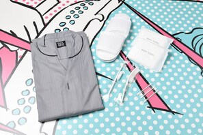 A neatly folded gray shirt, two white body towels, and a pink and white toothbrush set on a polka dot surface. - HOTEL TAVINOS Asakusa (Tokyo)