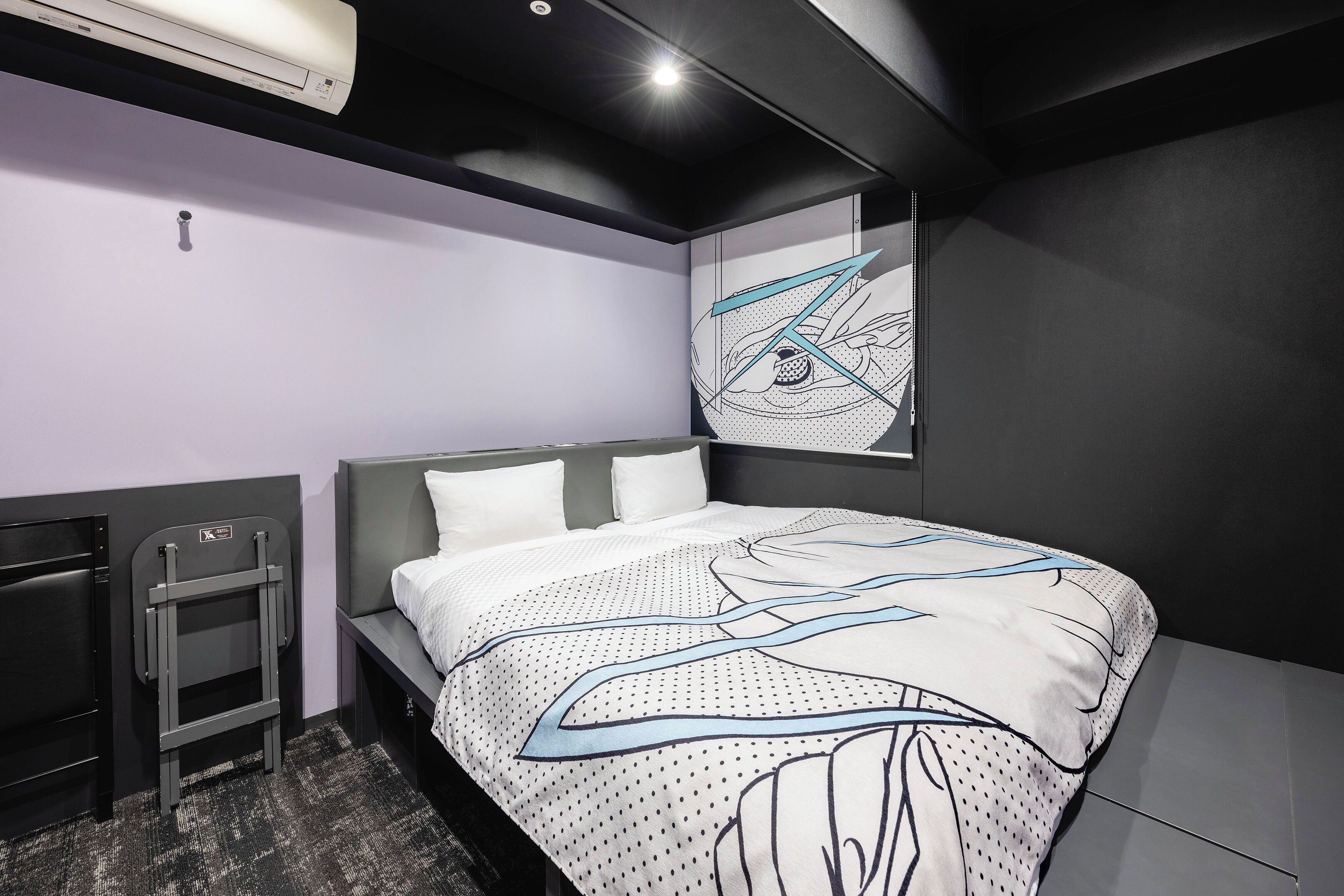 Una camera d'albergo moderna con un letto rifatto, una piccola scrivania e un'opera d'arte appesa al muro.
