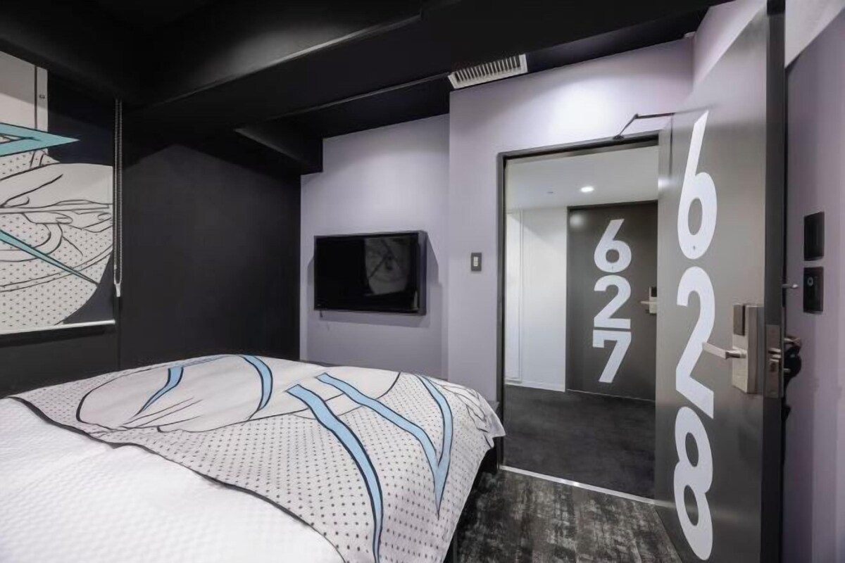 A modern hotel room with a bed, a door with a number, and a wall with a geometric design.