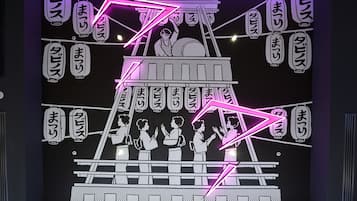 Un mur illuminé par des néons, orné de caractères japonais et d’une illustration stylisée représentant une scène traditionnelle.