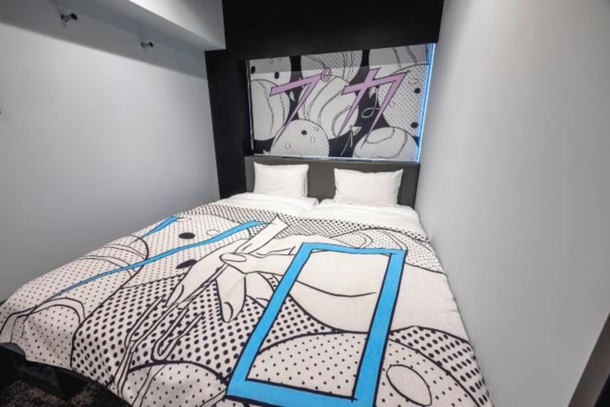 A bedroom with a bed featuring a comic-style patterned bedspread, a headboard with a large graphic, and white pillows.