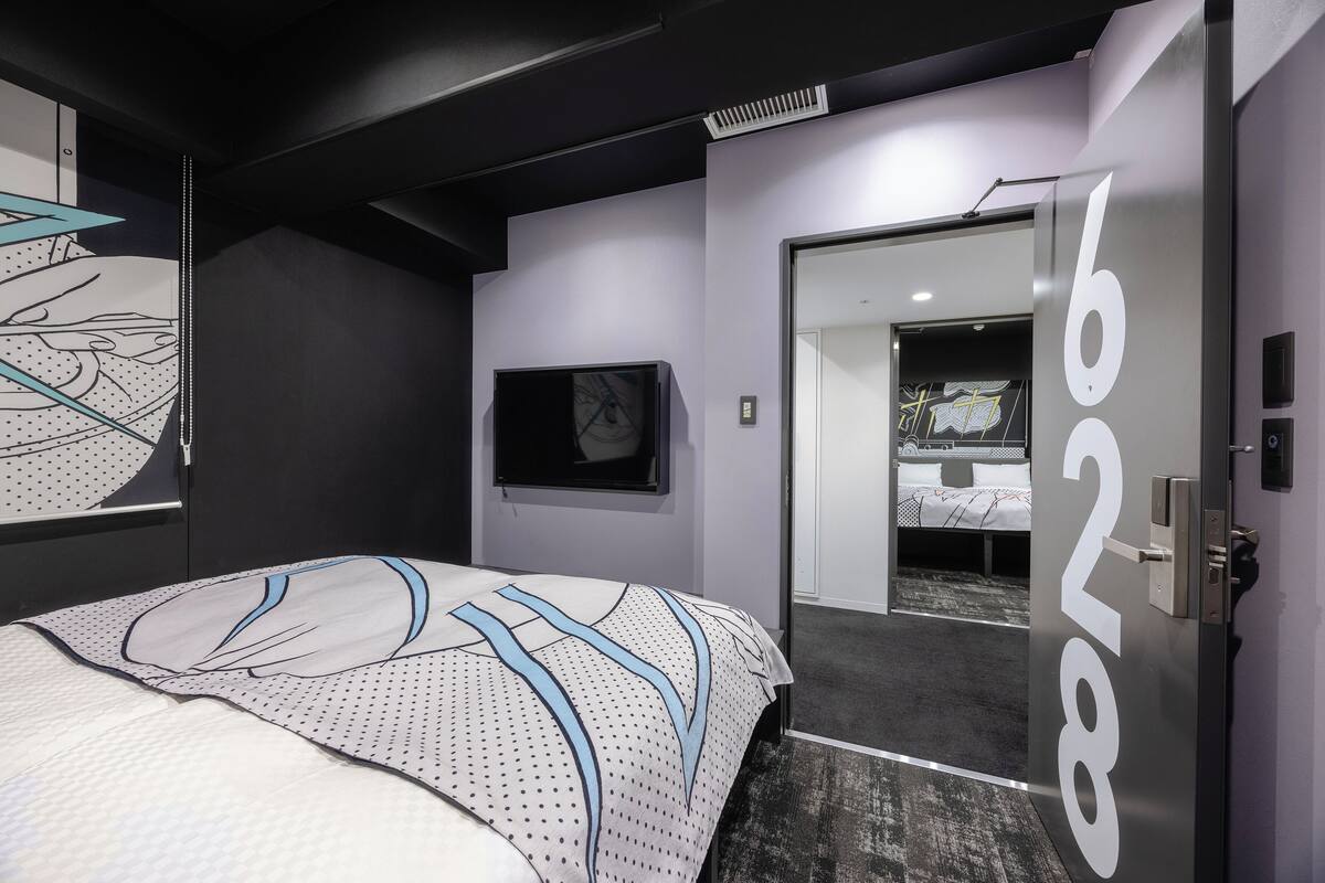 Une chambre d’hôtel moderne, dotée d’un grand lit, d’une petite fenêtre et d’une porte portant le numéro 622.
