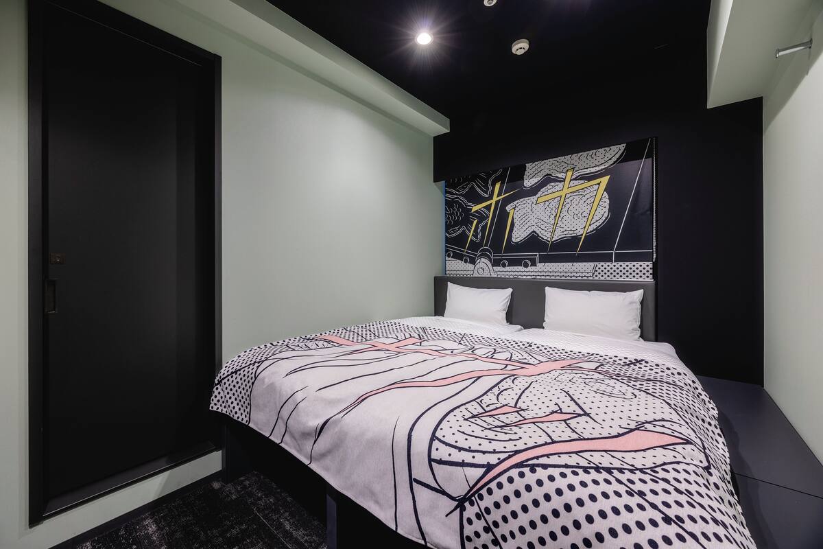 Une chambre à coucher avec un lit, une armoire sombre et un mur orné d’un motif graphique.