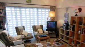 A living room with a television, two armchairs, a coffee table, and a bookshelf. - 44 Lodge And Suites (Lagos)