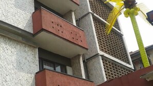A multi-story building with a textured facade, balconies with red railings, and a palm tree in the background. - 44 Lodge And Suites (Lagos)