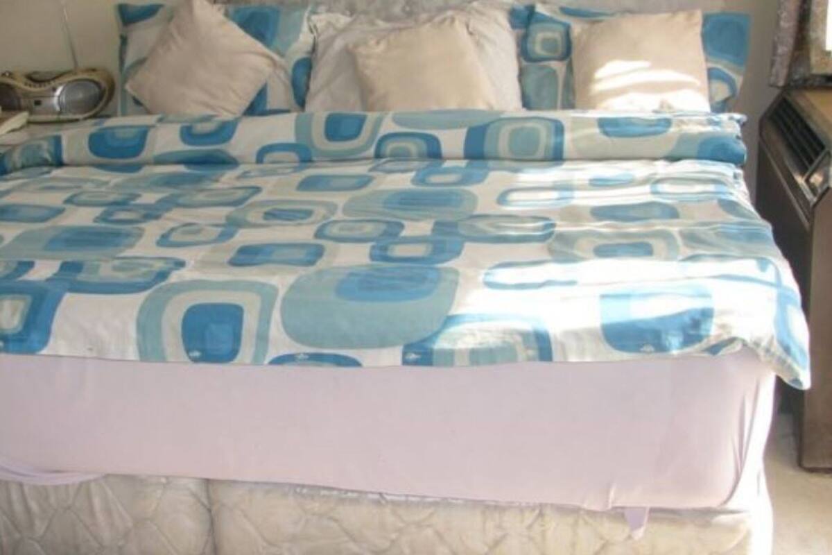A bed with a patterned bedspread, a bedside table with a radio, and a window with curtains.