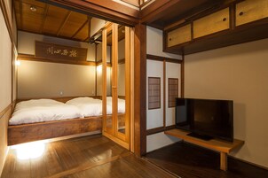Una habitación tradicional japonesa con una cama de madera, puertas correderas y un televisor sobre un soporte de madera.