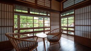 A traditional Japanese room with tatami flooring, sliding shoji doors, and a view of a green landscape. - KANSUIRO Annex (Hakone)