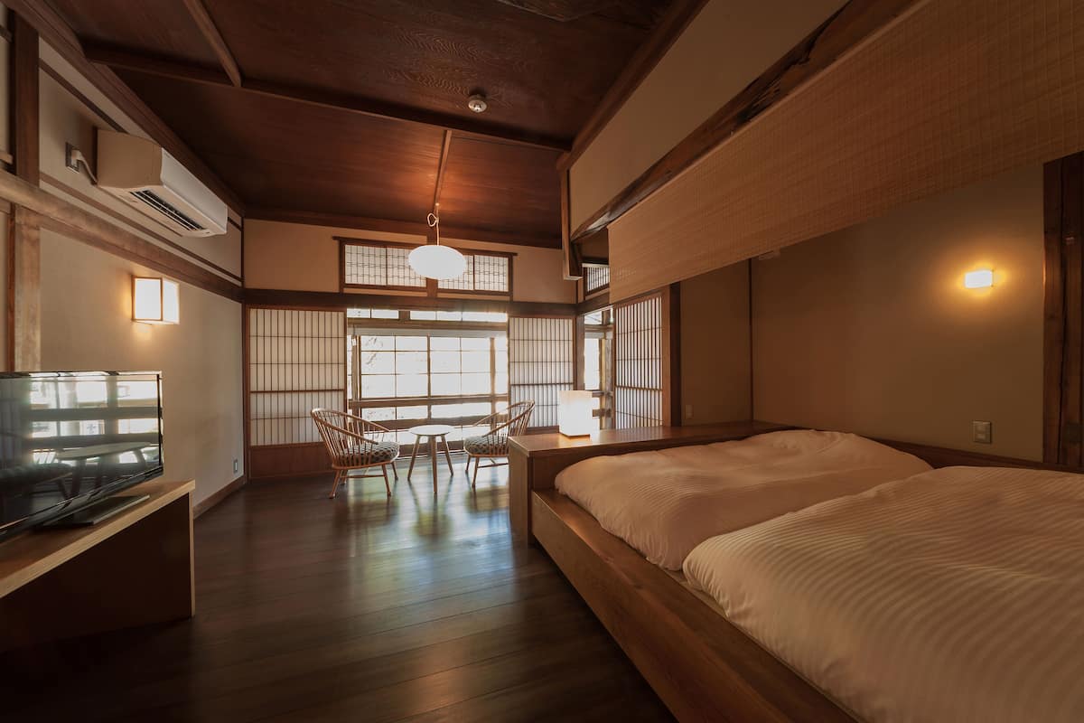 A traditional Japanese-style room with tatami flooring, a low wooden bed, a television on a wooden stand, and a sliding shoji screen door.