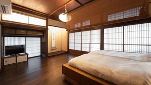 A traditional Japanese-style bedroom with tatami flooring, a low platform bed, a television on a cabinet, and large windows with shoji screens. - KANSUIRO Annex (Hakone)