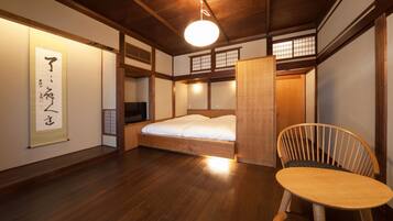 A traditional Japanese-style room with tatami flooring, a low wooden bed, a wooden chair, and a hanging shoji screen.